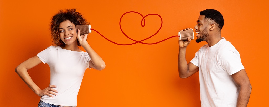 Photo of two people playing the telephone game in which they speak to each other through cans connected by a string that curls into a heart.