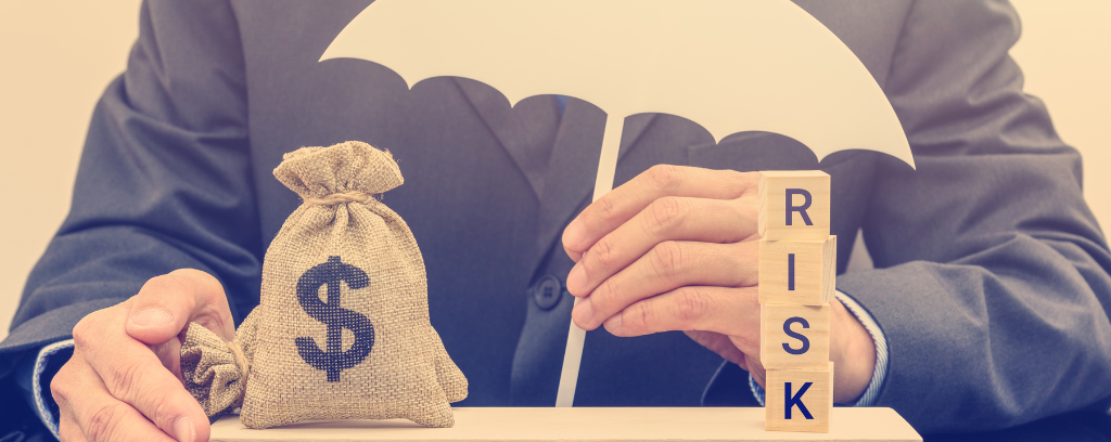 Photo of business owner holding umbrella over bag of money and blocks spelling risk