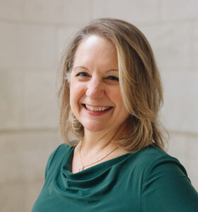 Nance Schick smiling and wearing green dress outside New York Public Library in Midtown Manhattan