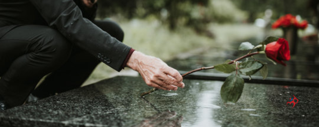 Photo of funeral director placing a red rose on a casket